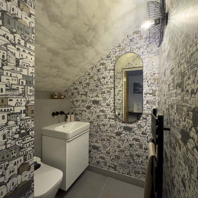 Small cloakroom with basin, wall-mounted toilet, patterned feature wallpaper, black taps, and black towel rail in a contemporary Sneyd Park home by Ivywell Interiors