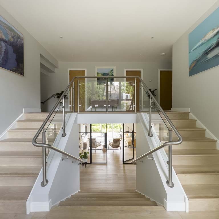 Contemporary entrance with double staircase featuring metal and glass balustrade and large colourful artwork in a Sneyd Park home by Ivywell Interiors