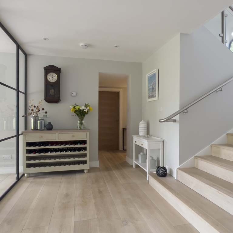 Contemporary hallway with light oak flooring, black Crittall-style doors, and a vintage wall clock in a Sneyd Park family home by Ivywell Interiors