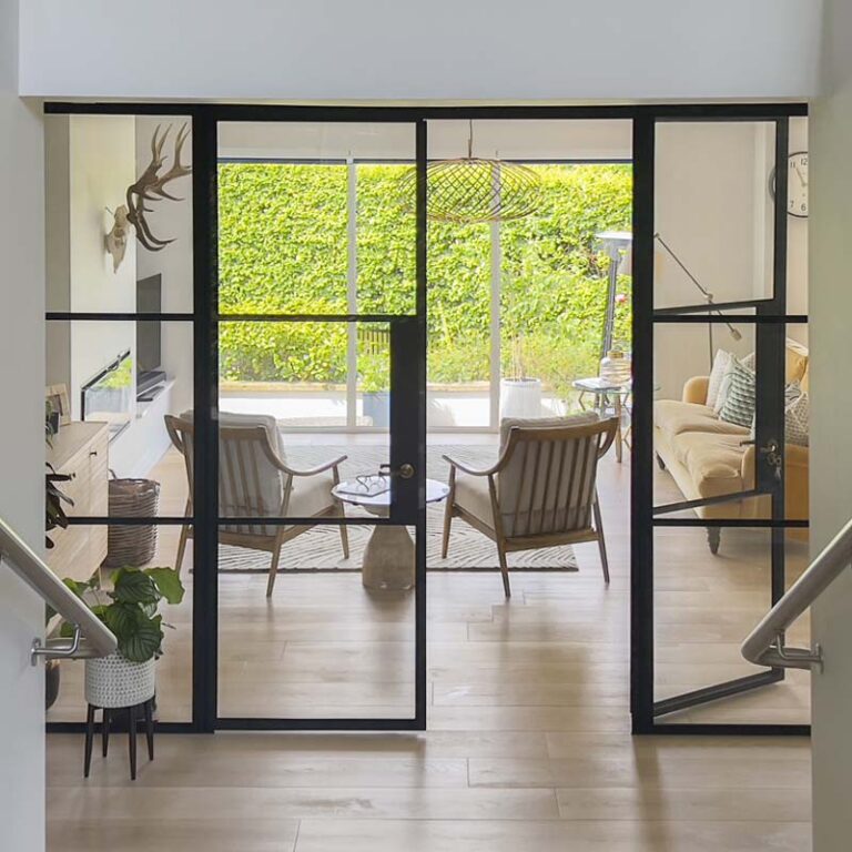 Large double Crittall-style doors with black metal frames opening onto a bright open-plan space in a Sneyd Park home by Ivywell Interiors