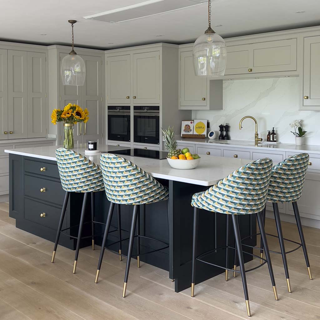 Shaker-style kitchen with large dark blue island, colourful upholstered stools, and brass detailing in a contemporary Sneyd Park family home by Ivywell Interiors