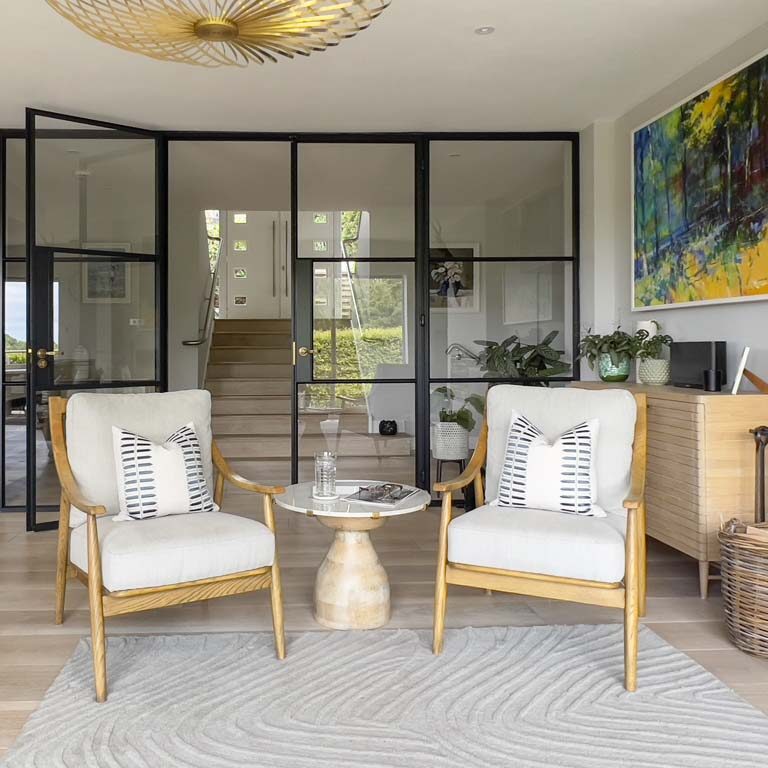 Detail of occasional armchair in an open-plan living space with large double Crittall-style doors in a contemporary Sneyd Park home by Ivywell Interiors
