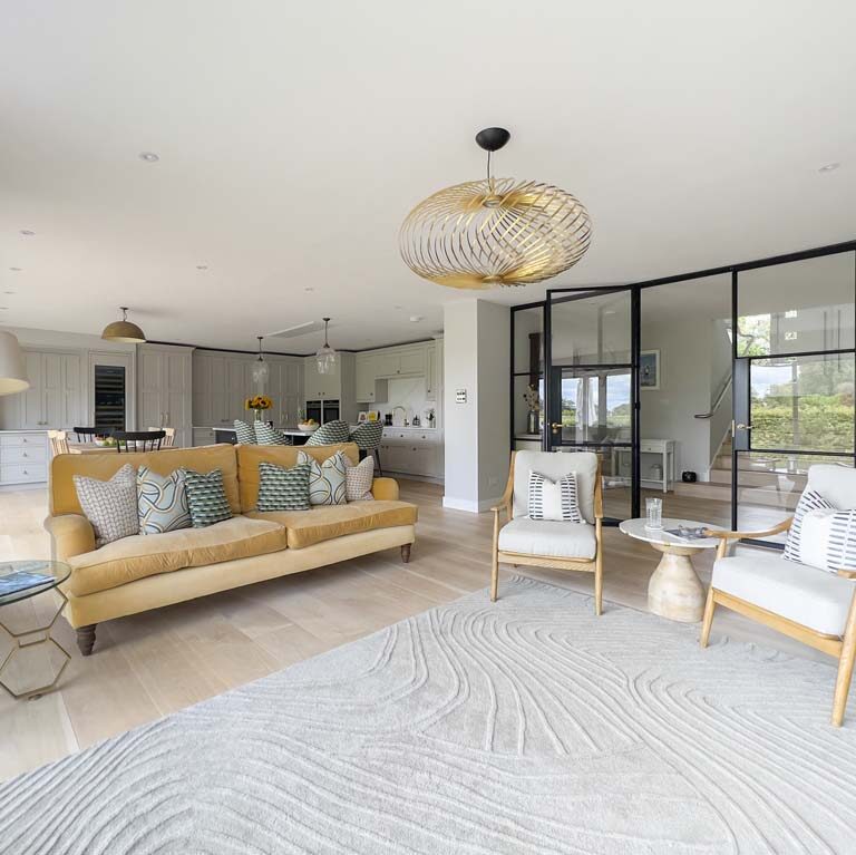 Open-plan kitchen and living room with mustard velvet sofa, large BoConcept rug, Tom Dixon light, Crittall-style double doors, and a shaker-style kitchen in a contemporary Sneyd Park home by Ivywell Interiors