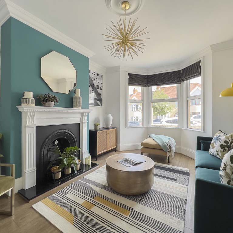 Living room with bay window, roman blinds, feature blue chimney breast, gold accent furniture, and large rug in a Bedminster townhouse by Ivywell Interiors