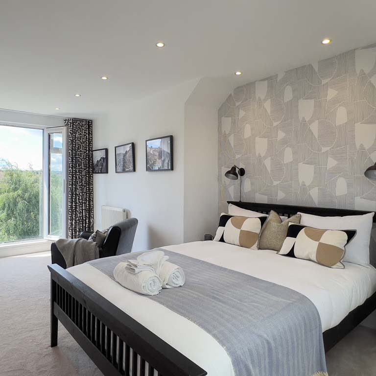 Loft master bedroom with a monochrome palette and feature wallpaper behind the headboard in a Bedminster townhouse by Ivywell Interiors