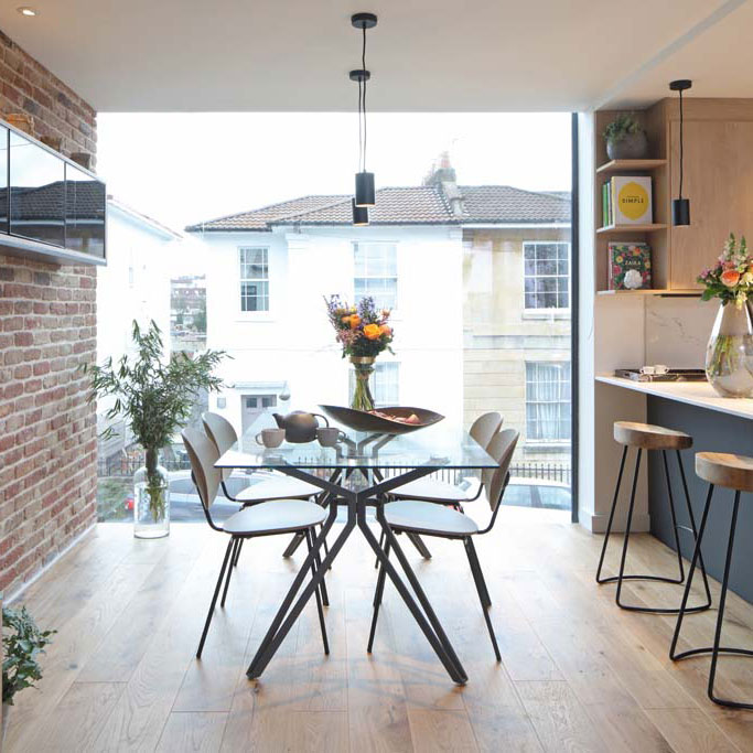 Open-plan dining room with exposed red brick wall and floor-to-ceiling profile-less window in a new-build home in Cotham by Ivywell Interiors