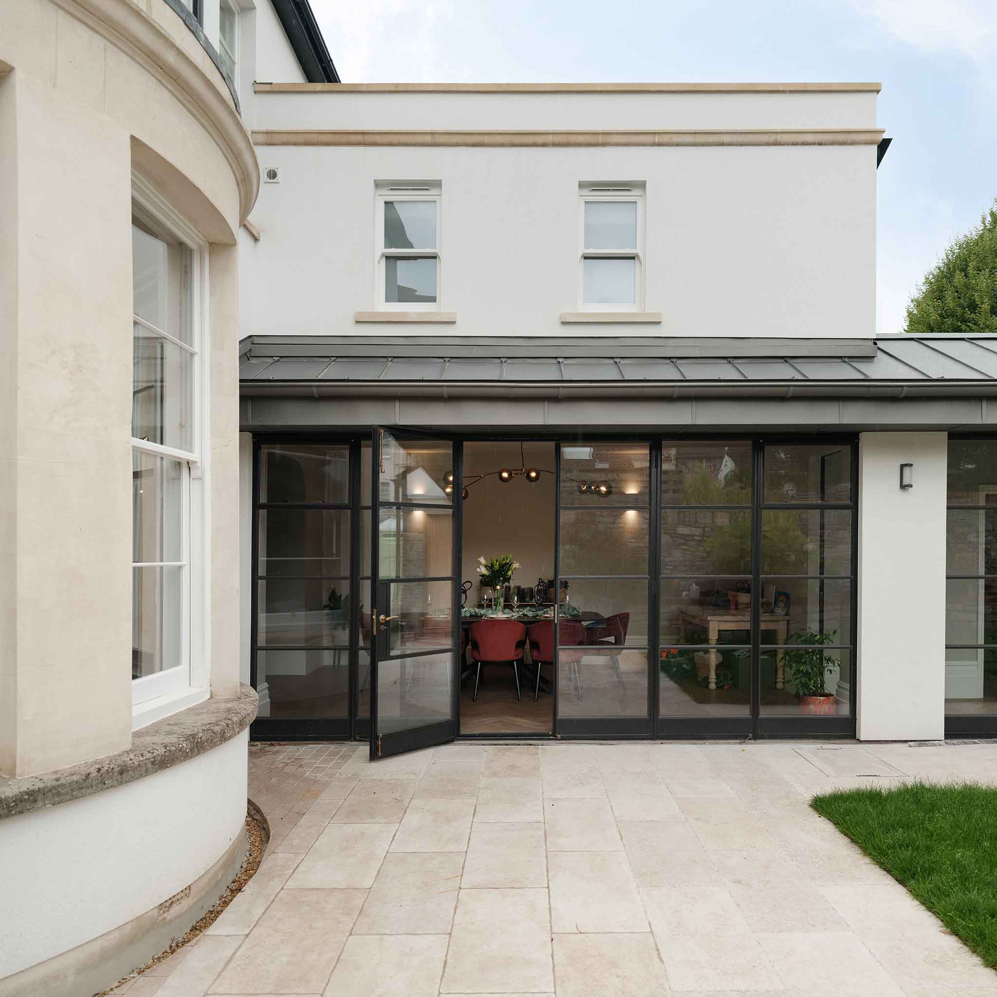 Rear view of a renovated Victorian family home in Redland, Bristol, featuring Crittall-style glass doors opening onto a modern stone patio with views into the dining room.