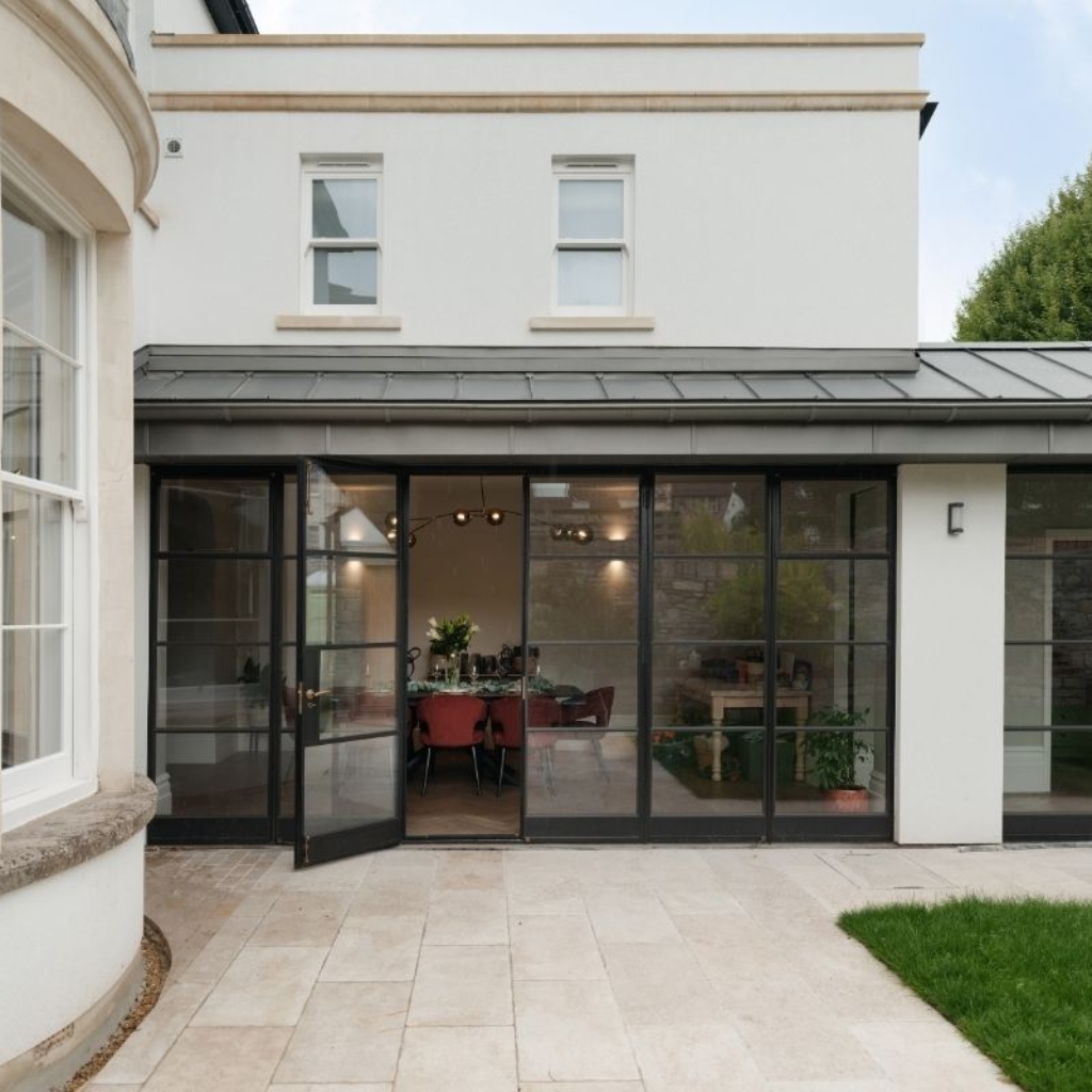 Rear view of a renovated Victorian family home in Redland, Bristol, featuring Crittall-style glass doors opening onto a modern stone patio with views into the dining room.