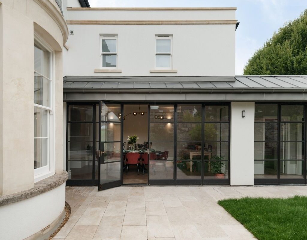 Rear view of a renovated Victorian family home in Redland, Bristol, featuring Crittall-style glass doors opening onto a modern stone patio with views into the dining room.