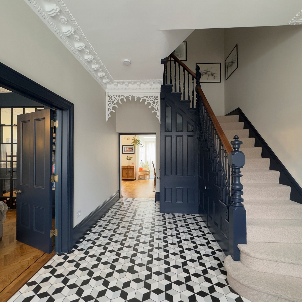 Hallway of period home featuring a geometric tiled floor, dark blue woodwork and carpeted stairs